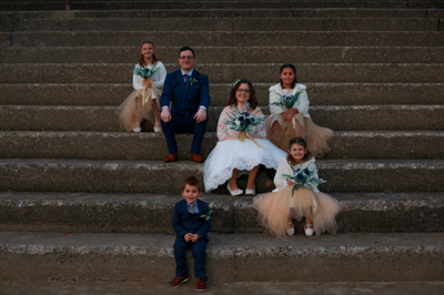 Swansea%20bay%20wedding%20photography%20-%20A%20bride%20and%20groom%20sit%20on%20steps%20surrounded%20by%20their%20bridesmaids%20and%20usher