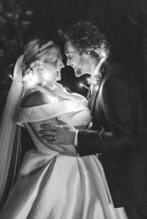 Black%20and%20white%20photo%20of%20a%20bride%20and%20groom%20lit%20up%20by%20string%20fairy%20lights%20lighting%20up%20their%20faces.